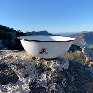 Hungry Hiker lightweight white enamel camping bowl on a rock overlooking mountain scenery.