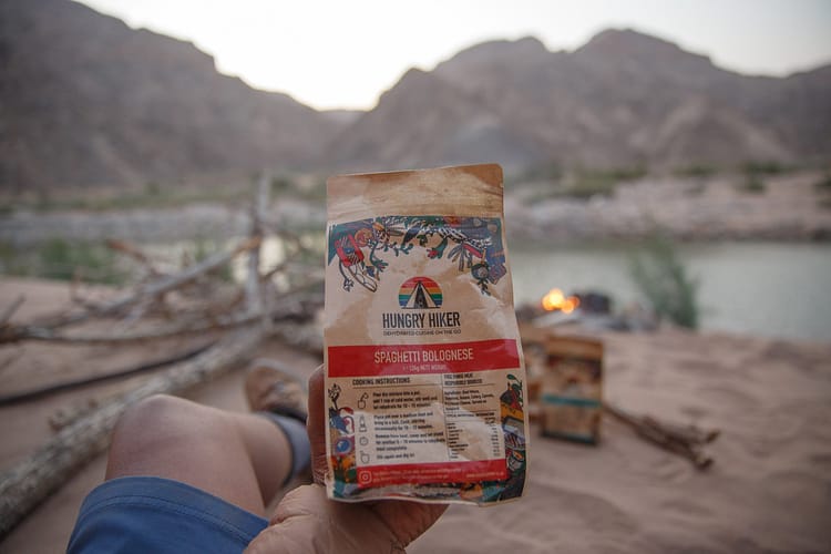 Hungry Hiker dehydrated hiking meal held at a campsite beside a river during a multi-day hike